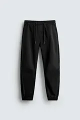 Pantalón jogger negro de corte slim fit, confeccionado en tejido de algodón con cintura elástica ajustable con cordón, bolsillos frontales y traseros, y puños elásticos en los tobillos.