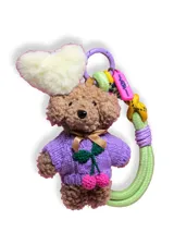 Llavero con forma de oso de peluche marrón con sweater tejido color lila, detalle de cerezas bordadas y corazón de peluche blanco.