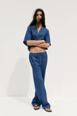 Camisa corta de denim azul, con cuello solapa, escote en pico y mangas cortas.
