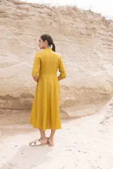 Vestido midi color mostaza, estilo camisero, con cuello mao, mangas 3/4 y cinturón trenzado.