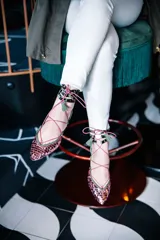 Bailarinas chatitas con punta cubierta de lentejuelas rosadas, laterales y talón de gamuza verde oliva, y tobillera de cuero con estampado animal print. Se atan al tobillo con cordones rosas y tienen un pequeño fleco decorativo en el talón.