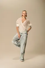 Pantalón de jean de tiro medio y corte recto, con lavado claro y aplicación de encaje floral blanco que cubre toda la prenda. Presenta roturas en las rodillas y muslos.