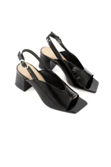 Sandalias de charol negro con punta cuadrada, tira delantera ancha y tira trasera con hebilla. Tacón bloque bajo.