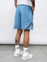 Bermuda deportiva negra de algodón y poliéster, con cintura elástica ajustable con cordón, bolsillos laterales y detalle de recortes geométricos en gris en los laterales. Logo de la marca bordado en la pierna izquierda.