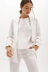 Blazer color beige confeccionado en lino, con cuello solapa, cierre frontal con un botón y mangas largas con volantes en capas.