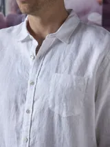 Camisa azul de lino con botones blancos, manga larga y bolsillo en el pecho.