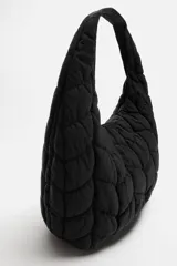 Bolso de hombro negro fabricado en tejido técnico acolchado con diseño geométrico. Tiene un compartimento principal con cierre mediante imán, un bolsillo plano y un bolsillo con cierre mediante cremallera en el interior.