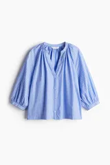 Blusa de popelina de algodón a rayas celestes y blancas, con cuello mao, abertura en V y botones frontales. Mangas globo tres cuartos de corte raglán con puños finos y bajo recto.