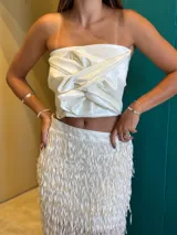 Top strapless color crudo con efecto satinado, caracterizado por un drapeado estructurado y un nudo frontal prominente.