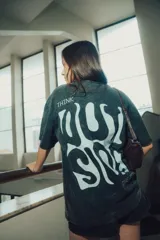 Remera de manga corta color gris oscuro con efecto gastado (acid wash). Estampado grande en la espalda con texto estilizado en blanco que incluye la palabra "THINK" arriba y un diseño abstracto debajo.