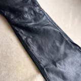 Pantalón de cuero negro, de corte recto y tiro alto, con bolsillos delanteros y traseros.