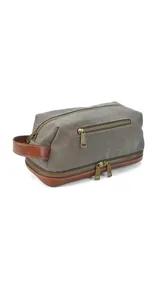 Neceser gris de tela canvas con detalles en cuero marrón. Tiene doble compartimento con cierre, bolsillo frontal con cierre y asa lateral de cuero.