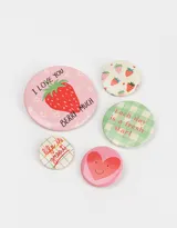 Set de cinco pines redondos con diferentes diseños: fresa con texto "I love you berry much", corazón sonriente, texto "Life is great" sobre fondo a cuadros, fresas sobre fondo crema, y texto "Each day is a fresh start" sobre fondo a cuadros verde y blanco.