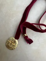 Gargantilla de terciopelo color borgoña con dije dorado con la figura del Espíritu Santo.