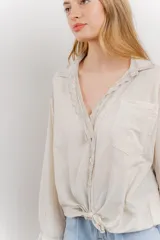 Camisa color crema de manga larga con cuello camisero y detalles de encaje en el escote. Se ata en la parte delantera.