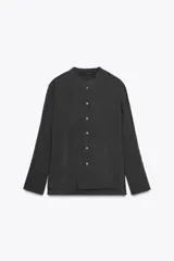 Camisa negra de lyocell con cuello redondo, manga larga con puños y bajo asimétrico con aberturas laterales. Cierre frontal con botones.