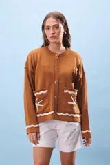 Cárdigan marrón de tejido de punto con cuello redondo y cierre frontal con botones. Tiene bolsillos frontales con diseño de olas y estrellas de mar en color blanco.