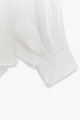 Camisa blanca de lino con cuello clásico, manga larga con puños abotonados y bajo asimétrico.