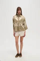 Camisa blanca con estampado de palmeras en color azul marino, de corte holgado, con cuello camisero, cierre frontal con botones y mangas 3/4 con puños anchos.