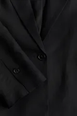 Blazer negro de lino y viscosa con solapas de pico, hombreras finas y cierre de un botón. Modelo entallado con pinzas en la cintura, abertura con botón en los puños y bolsillos delanteros ribeteados. Abertura atrás y forro interno.