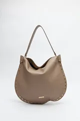 Bolso hobo color beige de símil cuero con textura suave y tachas metálicas en los bordes. Tiene correa al hombro y logo metálico en el frente.