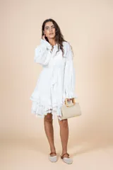 Vestido corto blanco de tela liviana con textura suave, escote en V con lazo, mangas largas amplias y volados en el ruedo.