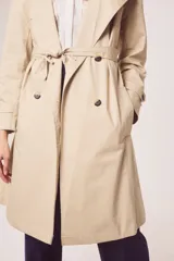 Trench color beige con doble botonadura, cinturón y cuello clásico.