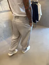 Pantalón de vestir de corte sastrero holgado (oversize) color gris claro, con pliegues frontales y cierre de cremallera.