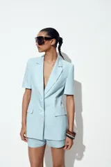 Blazer celeste de lino con cuello solapa, manga corta con hombreras, bolsillos delanteros con solapa, cintura entallada y cierre frontal con botones.