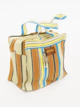 Bolso playero tipo tote bag a rayas horizontales en tonos naranja, amarillo, blanco y violeta. Tiene doble asa corta y cierre superior con cremallera. Incluye un dije colgante y una etiqueta de cuero sintético con el logo de la marca.