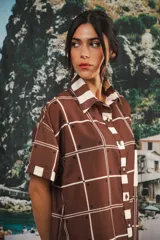 Vestido camisero corto con estampado a cuadros en tonos beige, rojo y azul. Tiene cuello camisero, botones frontales, bolsillo en el pecho y corte recto.