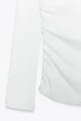 Camiseta negra de algodón con escote recto, hombros descubiertos y mangas largas. Presenta detalle de frunces en el frente.