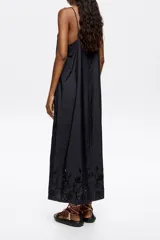 Vestido midi negro de corte recto y fluido, con escote pico pronunciado y tirantes finos. Presenta bordado inglés con motivos florales en el escote, laterales y ruedo.