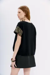 Remera de jersey 100% algodón color blanco, con cuello redondo y manga corta caída. Las mangas están completamente bordadas con lentejuelas tono sobre tono.