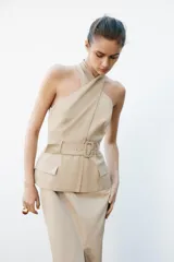 Vestido midi color beige con cuello halter cruzado, cinturón con hebilla y bolsillos tipo parche.