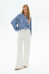 Blusa con estampado de hojas en azul y blanco, de tejido liviano, con cuello corto fruncido y tapeta de botones. Mangas globo largas con volumen de corte raglán y puños finos abotonados.