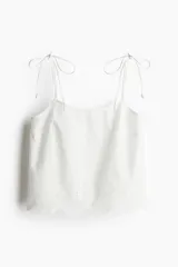 Top blanco de algodón con breteles finos que se atan en moño y ribete festoneado bordado en el bajo.