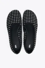 Zapato tipo bailarina color negro, con acabado en punta redonda y suela plana. Diseño de rejilla con tachas plateadas en todo el cuerpo.