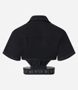 Camisa corta negra con cuello camisero, mangas cortas y aberturas laterales con elástico con letras blancas.