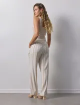 Pantalón de lino a rayas verticales color beige y blanco, con pretina ancha elastizada, lazo de ajuste y bolsillos inclinados.