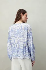 Blusa estampada celeste y blanca de caída fluida con cuello redondo y lazos frontales. Diseño con cortes horizontales y frunces, mangas largas con puños elastizados.