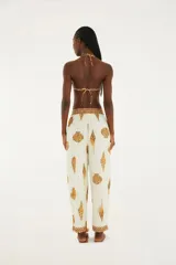 Pantalón de corte recto con estampado de conchas marinas en tonos marrones sobre fondo blanco. Presenta cintura elástica ajustable con cordón y borlas, bolsillos laterales y dobladillo con detalle de ribete marrón.