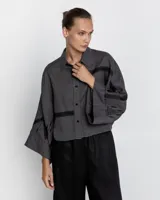Camisa gris con bordados negros, de corte holgado y mangas anchas.