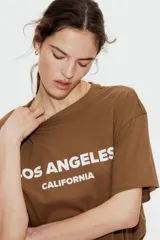 Remera color marrón con estampado blanco con la frase 'Los Ángeles California'. Corte recto y holgado, mangas cortas y cuello redondo.