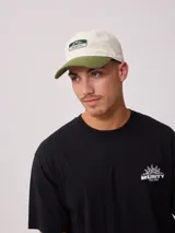 Gorra de lona lavada color beige con visera verde y parche con el logo de Rusty en el frente.