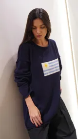 Sweater de tejido de punto color gris oscuro, con cuello redondo y mangas largas holgadas. Presenta un parche tejido en el pecho con la bandera de Uruguay.