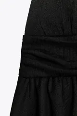 Top negro de cuello halter y escote pico con volantes en el bajo.