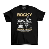 Remera negra con estampado de Rocky Balboa y Apollo Creed en el ring, con texto dorado que dice "Rocky", "The Rematch of the Century" y "Balboa v Creed".