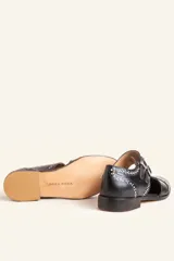 Zapato tipo monk strap con aberturas laterales, confeccionado en cuero vacuno color bordó. Presenta doble tira con hebillas metálicas plateadas en el empeine y suela de cuero con taco bajo.