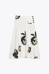 Falda midi de tiro alto confeccionada en hilatura de algodón color blanco con estampado floral en negro y amarillo. Tiene cierre con cremallera oculta en la costura y detalle de botones en la cintura.